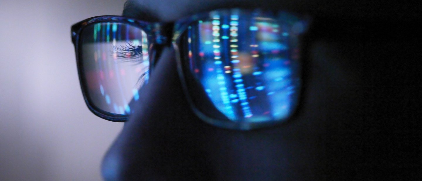 A luminous screen is reflected in the glasses of a man