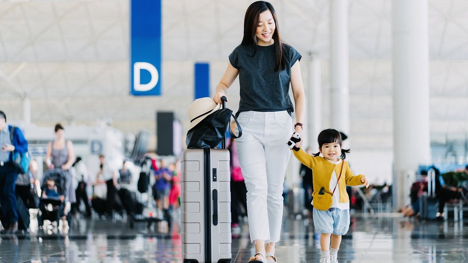 Joyful mother holding hands of her daughter, walking through airport concourse and traveling by plane on a vacation.