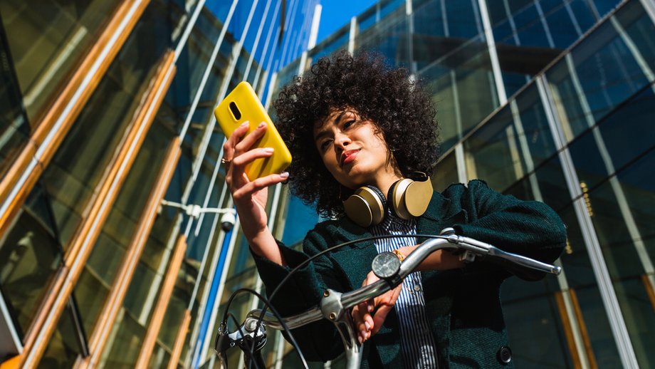 A woman sitting on a bike in the city holding a mobile in her hand
