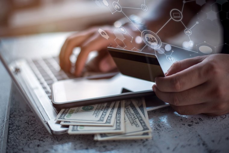 Shows online payment security with a side view of male hands holding credit card typing numbers on computer keyboard while sitting at home soft focus, flare sun light, cross process image