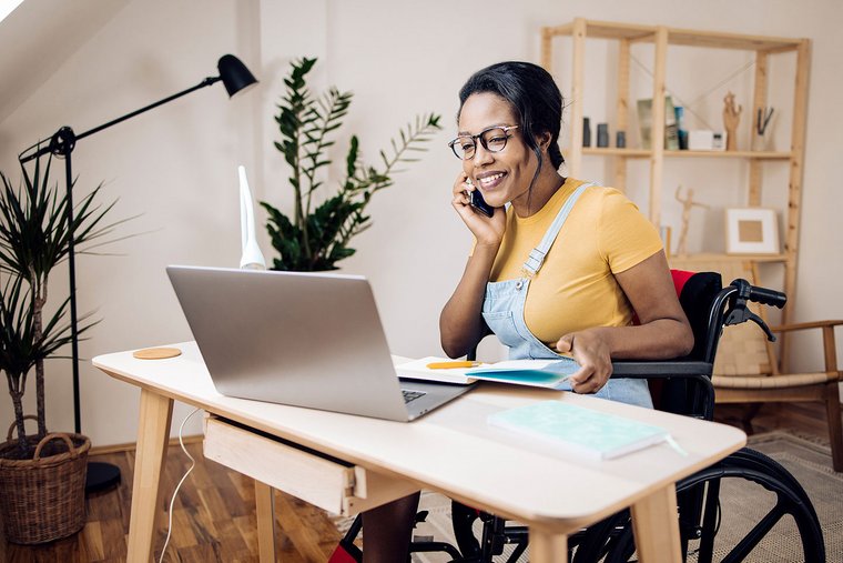 Young African American businesswoman using a wheelchair, working online, and telephoning from home.