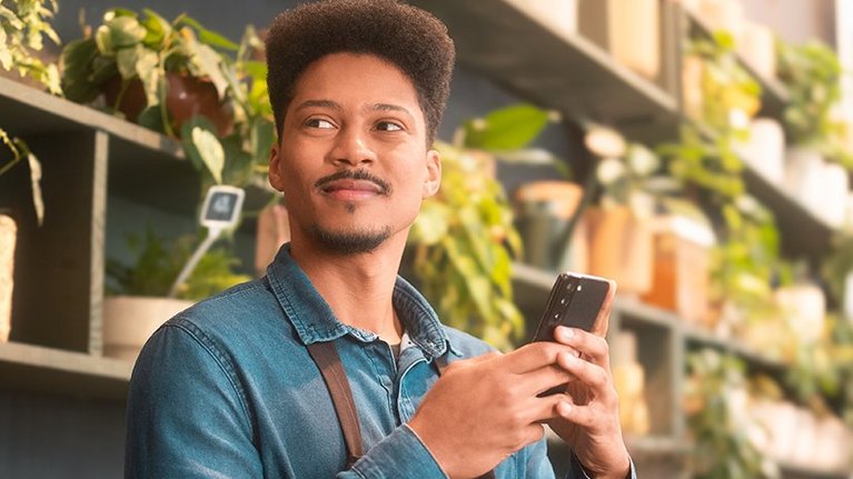 A young man holding a smartphone in a plant shop