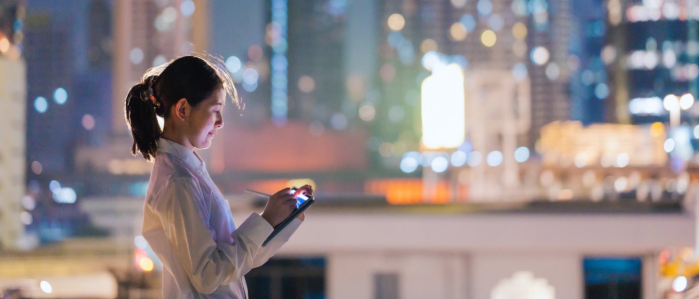 A woman using a tablet in front of the skyline of a city