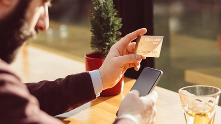 A man sits outside and operates his smartphone. In the other hand he holds a credit card