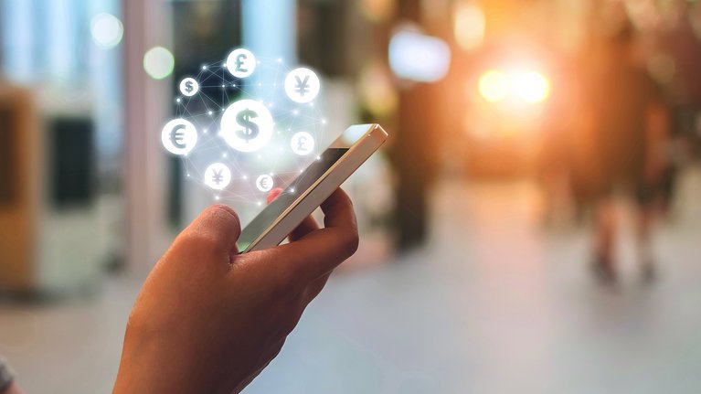 Someone operates a smartphone with symbols for various currencies hovering above it