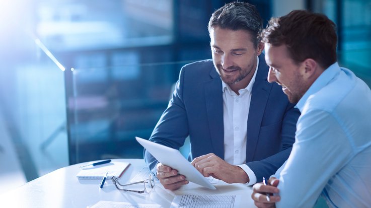 Two business men sitting together holding and discussing what they see on the tablet