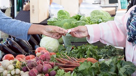 A bill is handed over to pay at a vegetable stall