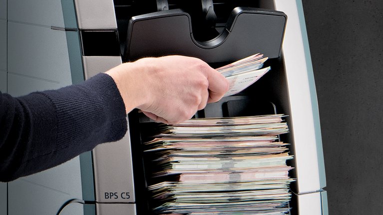 Someone loads the BPS® C5 banknote processing system with euro banknotes