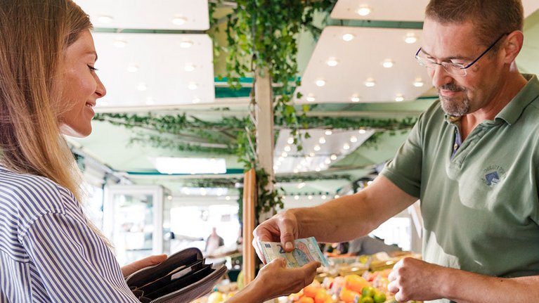 A woman pays with banknotes at a vegetable market stall