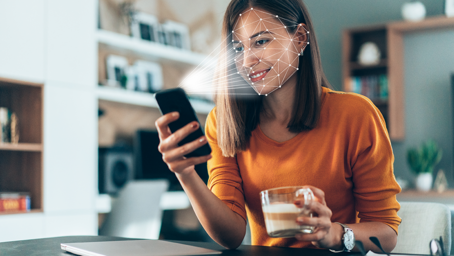 A woman sitting at a table using a smartphone that scans and authenticates her.
